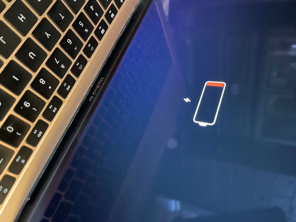 MacBook laptop displaying battery health status on screen with charging cable connected